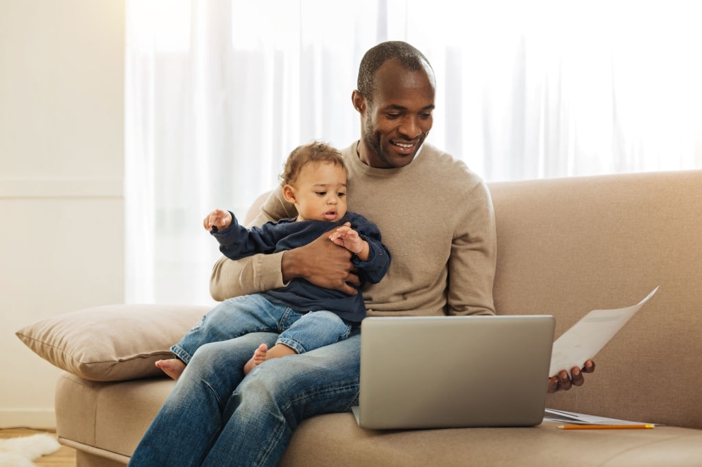 man carrying his son in front of a laptop